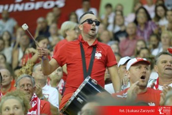 kibic wymalowany w biało czerwone barwy kibicuje zawodniczkom uderzając w bęben zawieszony na szyji w rytm muzyki